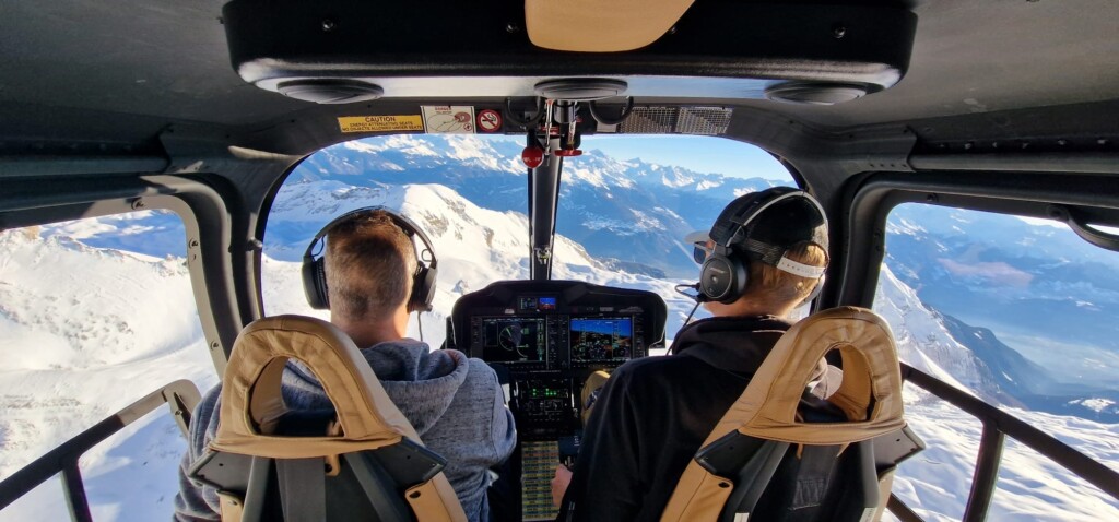 Image prise depuis l’intérieur du cockpit d’un hélicoptère pendant un vol d’initiation au-dessus des montagnes, illustrant la première expérience de pilotage proposée par le Chablais Heli Club